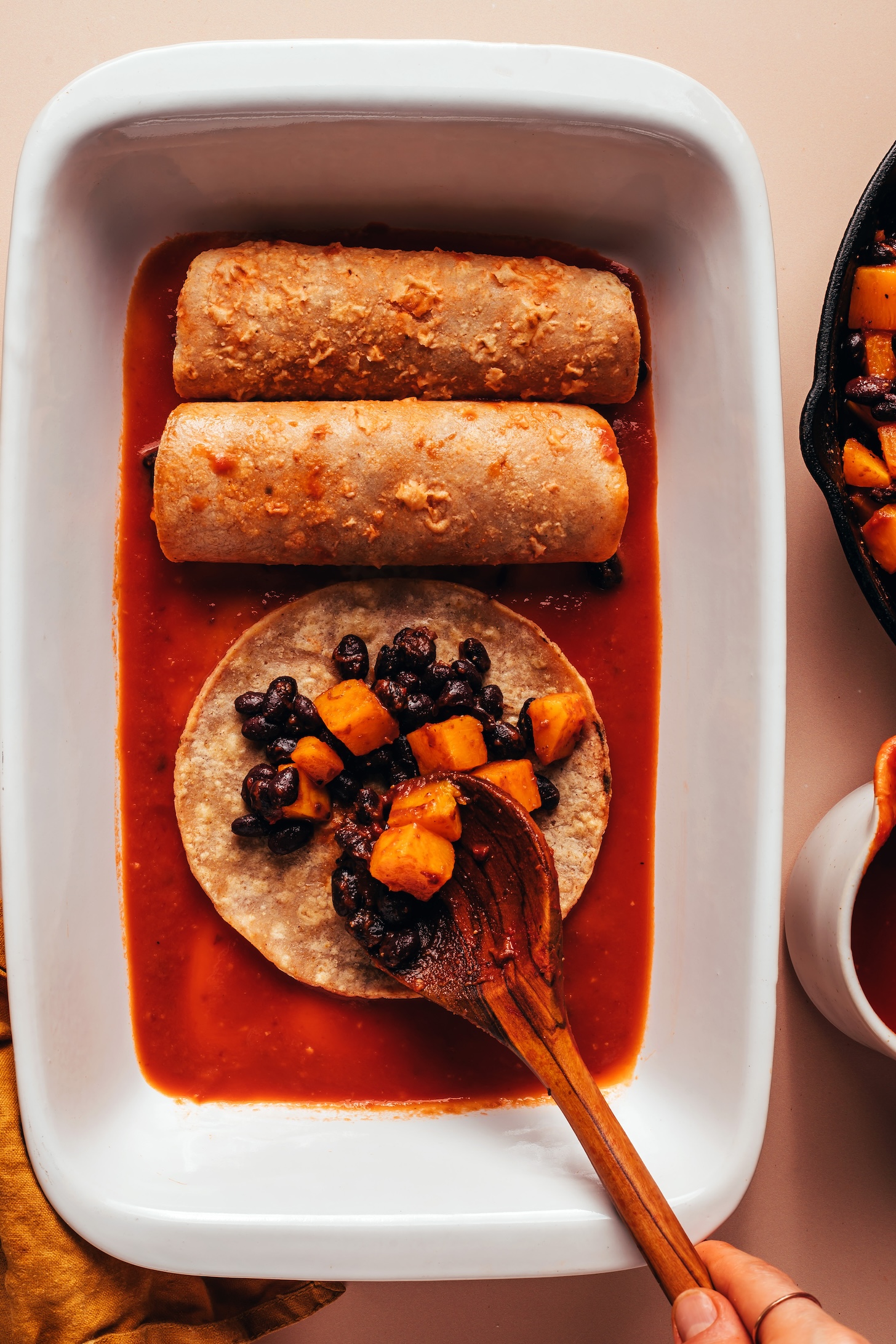 Using a wooden spoon to add a butternut squash and black bean filling on top of a corn tortilla